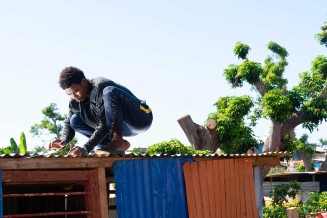 Laura Henno, "Un jeune cloue une tôle de son banga. Quartier informel de Barakani, Mayotte" © Laura Henno