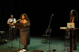 Kiyemis qui lit un texte avec des musiciens derrière elle