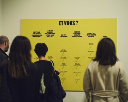 Photo d'ambiance du vernissage de l'exposition "Migrations & climat". Personnes devant un panneau avec l'inscirption : "Et vous ?"